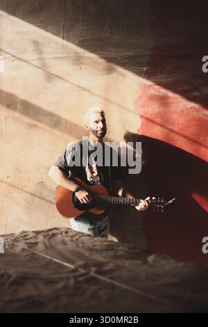 Musicista che suona la chitarra in una stanza illuminata dal sole con sottofondo artistico Foto Stock