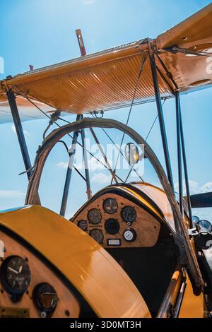 Vista interna dell'abitacolo di un biplano giallo d'epoca che mostra il quadro strumenti in legno con indicatori, dettagli di controllo e puntoni di supporto. L'angolo l Foto Stock
