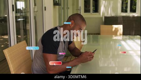 Un uomo di mezza età sorridente che tocca lo smartphone sul tavolo in vetro nel patio coperto, con sedie in vimini Foto Stock