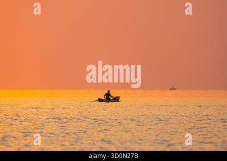 Vista di una figura solitaria che scivola sull'acqua in una piccola barca, illuminata dal caldo bagliore del sole che tramonta, Ngala, Lago Malawi, Malawi. Foto Stock