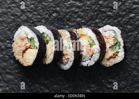 Sushi roll disposti in fila su sfondo in pietra nera. Sushi giapponese maki con nori di riso e ripieno di pesce. Composizione minima degli alimenti. Cugine asiatica. Foto Stock