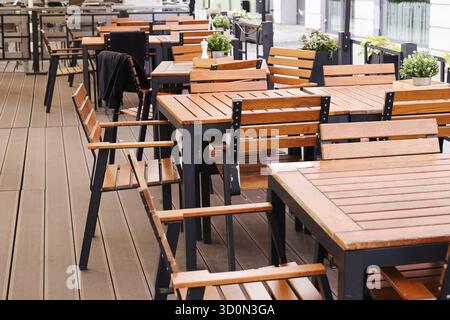 Terrazza vuota all'aperto con tavoli e sedie in legno. Moderna area salotto caffetteria. Non c'e' spazio per mangiare. Concetto di ospitalità urbana. Foto Stock