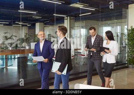 Professionisti che camminano insieme attraverso un moderno corridoio di vetro Foto Stock