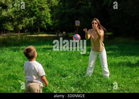 Mamma e bambino giocano a palla insieme nella natura durante le vacanze estive. Giocare a palla con il figlio nel parco. Palla presa Foto Stock