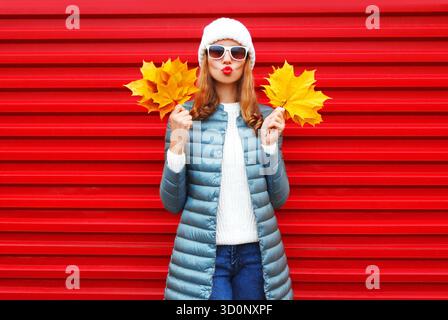 Donna autunnale alla moda con foglie d'acero gialle su sfondo rosso in città || modello rilasciato Foto Stock