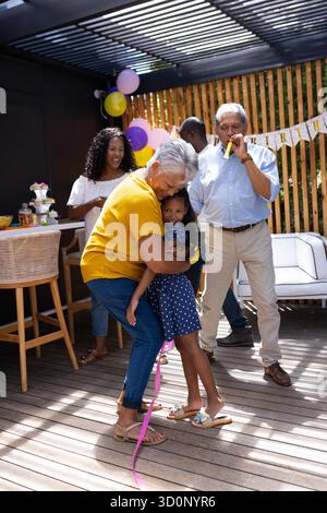 Nonna che abbraccia la nipote alla festa di compleanno, la famiglia festeggia gioiosamente insieme. Celebrazione, felicità, legame, multigenerazionale, insieme || modello rilasciato Foto Stock
