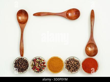 Interessante assortimento con varie spezie aromatiche e condimenti in piccole ciotole trasparenti e cucchiai di legno su sfondo bianco. Utilizzo per il sito Web, Foto Stock