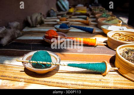 Filati colorati filati a mano su mandrini in legno, esposti con coloranti e fibre naturali, che mostrano la tradizionale lavorazione tessile in una luce vivace. Foto Stock