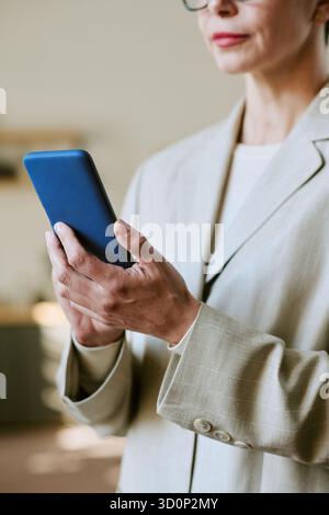 Donna di mezza età che usa lo smartphone mentre è in piedi in casa Foto Stock