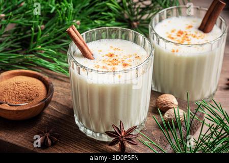 Bevanda all'eggnog (cocktail con latte d'uovo speziato) con cannella per Natale e le vacanze invernali. Eggnog fatto in casa in bicchieri con rami di pino. Foto Stock