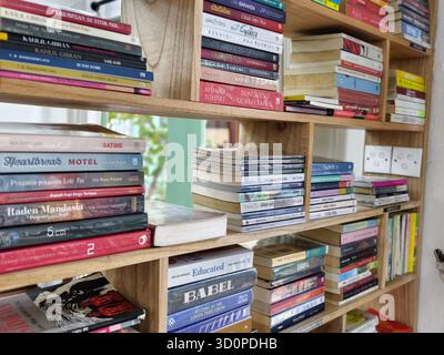Denpasar, Bali, Indonesia – 23 ottobre 2025: Una raccolta di libri su scaffali di legno in una libreria o in una biblioteca Foto Stock