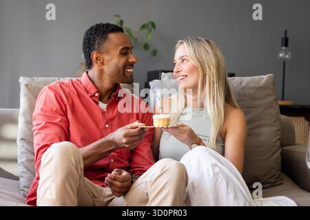 Festeggiare con il cupcake, coppia sorridente sul divano, condividere momenti speciali insieme. Festeggiamenti, dessert, felicità, relazione, amore, Joy || modello rilasciato Foto Stock