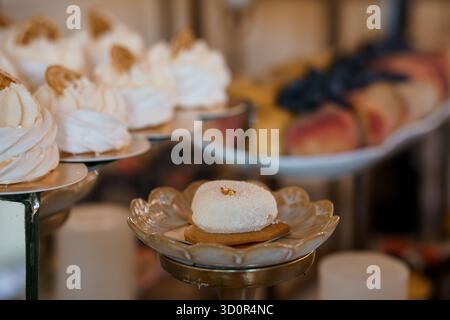 Un primo piano presenta lastricati bianchi splendidamente decorati adornati con foglie d'oro, disposti su piatti d'argento a più livelli durante un ricevimento di nozze. lussuosa Foto Stock