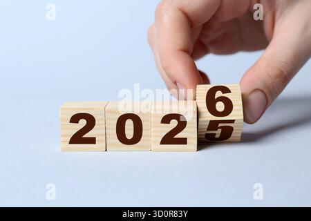 Anno nuovo. Donna che capovolge il cubo con i numeri 5 e 6 per fare 2026 su sfondo grigio, primo piano Foto Stock