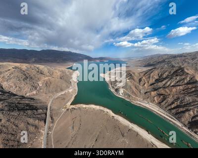 Ampia vista aerea di un vivace bacino idrico turchese che si estende attraverso un'ampia e arida valle di montagna sotto un cielo spettacolare con nuvole sparse Foto Stock