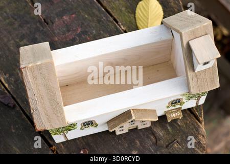 Un'affascinante scatola di legno progettata come una casa stravagante con dettagli dipinti, annidata su una superficie in legno intemprata sotto la luce naturale. Foto Stock
