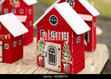 Primo piano di affascinanti case in legno rosso in miniatura con tetti bianchi, decorazioni natalizie e piccoli alberi in vaso, creando un accogliente villaggio natalizio Foto Stock