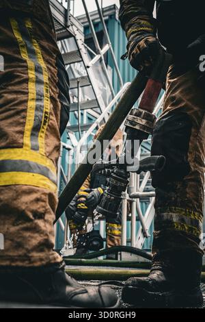 I vigili del fuoco indossano indumenti protettivi che utilizzano tubi dell'acqua durante uno scenario di addestramento antincendio. Foto Stock
