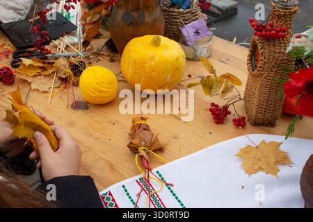 Fare decorazioni di Halloween. Una ragazza sta facendo una rosa con foglie d'acero. Piccole zucche sono sul tavolo e un vaso di frutti di bosco di rowan si trova nelle vicinanze. Foto Stock