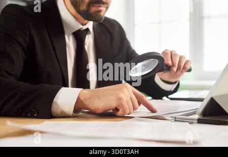 Primo piano di un uomo d'affari che controlla i documenti e rivede i dati con una lente di ingrandimento Foto Stock