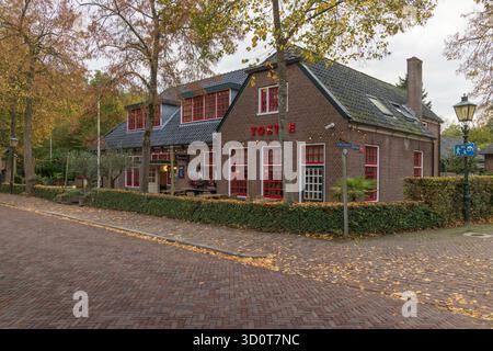 Vista d'angolo della "De Vierde Gang" a Haarzuilens, un tradizionale edificio in mattoni con cornici rosse alle finestre, circondato da alberi autunnali e fogliame. Foto Stock
