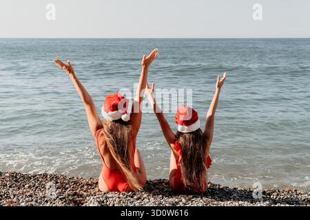 Due donne in Babbo Natale Cappelli che si godono la spiaggia Foto Stock