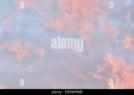 Un'atmosfera da sogno in cui una massa drammatica di nuvole di rosa e pesca si illumina contro una malva pallida e il cielo blu durante il tramonto o l'alba, riempiendosi Foto Stock
