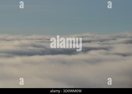 Una vista panoramica da un aeroplano mostra una vasta distesa di morbide e soffici nuvole sotto un cielo blu brillante. La luce del sole illumina le nuvole, creando un Foto Stock