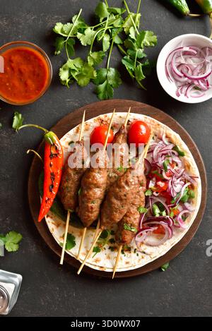 Kebab lula alla griglia con verdure fresche su pane piatto su un piatto di legno su sfondo scuro. Vista dall'alto, piano orizzontale, primo piano Foto Stock