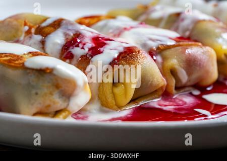 Pancake fritti ripieni di formaggio fresco e ciliegia, dessert dolce sul piatto, primo piano. Cottura fatta in casa. Ottimo fast food a colazione. A. Foto Stock