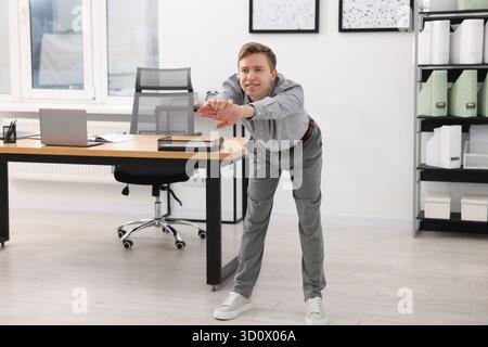 Giovane uomo d'affari che fa esercizio di stretching in ufficio Foto Stock
