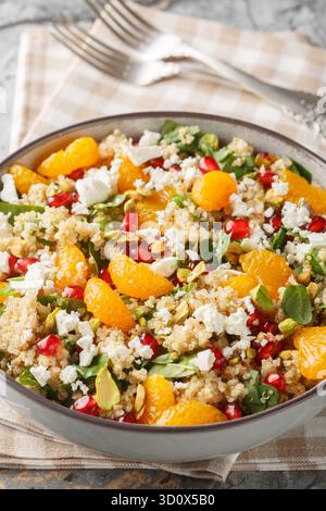 Insalata di quinoa con spinaci, feta, mandarini, melograno e pistacchi, primo piano in un recipiente sul tavolo. Verticale Foto Stock