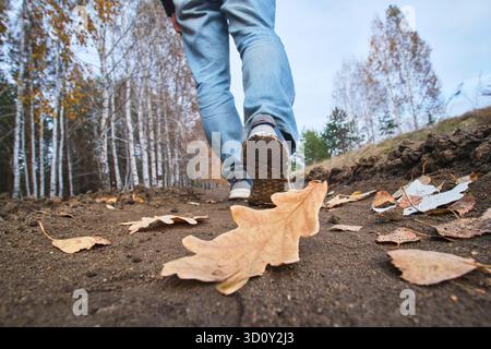 L'uomo cammina lungo il sentiero in una foresta autunnale attraverso foglie cadute. Primo piano Foto Stock