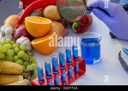 Scienziata donna che esamina frutta e verdura fresche con una lente d'ingrandimento in un laboratorio. Foto Stock