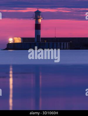 Un tramonto suggestivo dipinge il cielo con colori vivaci sopra il faro di Höganäs, Svezia. La luce calda si riflette sulle acque tranquille dell'ha Foto Stock