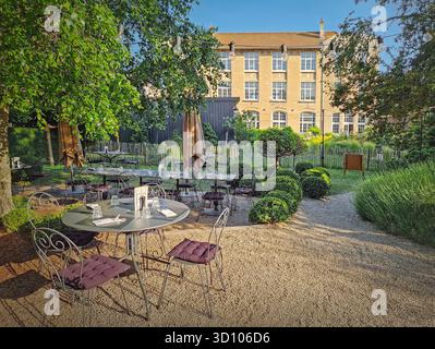 Terrazza ristorante rustica all'aperto con un'estetica classica ed europea del giardino. L'area salotto presenta tavoli da bistrot rotondi disposti su un sentiero di ghiaia. Strin Foto Stock