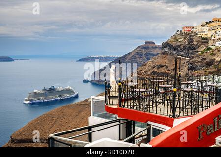 Una statua greca sul bordo di una terrazza che si affaccia sul Mar Egeo e sulla Caldera, con la città collinare e la nave da crociera in vista a Fira, Santorini, Grecia. Foto Stock
