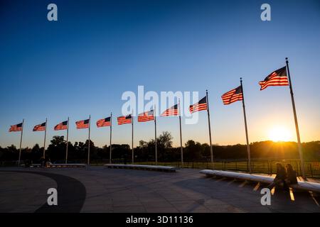 Washington Monument Flags al tramonto Washington DC // WASHINGTON DC - Una fila di bandiere americane vola contro il tramonto sul National Mall di Washington D.C., creando un bagliore dorato e ombre prominenti. Questa zona significativa ospita numerosi monumenti e memoriali nazionali, tra cui il vicino World War II Memorial. Amministrato dal National Park Service, il National Mall funge da punto di ritrovo centrale per eventi pubblici e dimostrazioni. Foto Stock