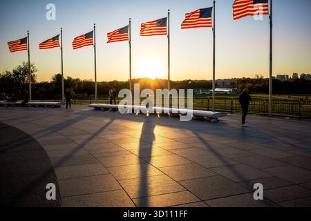 Bandiere americane al tramonto Washington DC // WASHINGTON DC - le bandiere americane sono inondate dalla luce del sole dorata appena prima del tramonto sul National Mall. Il sole basso proietta lunghe ombre in primo piano sull'area pavimentata, creando un effetto drammatico. Sullo sfondo, il Lincoln Memorial Reflecting Pool e il Lincoln Memorial sono visibili, iconici monumenti storici nella capitale della nazione. Quest'area è un luogo significativo per i monumenti nazionali e le riunioni pubbliche. Foto Stock