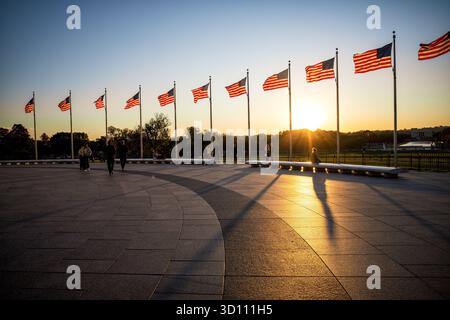 American Flags al tramonto Washington DC // WASHINGTON DC - le bandiere americane volano al National World War II Memorial, un importante punto di riferimento sul National Mall, durante il tramonto. Questo memoriale onora i 16 milioni di americani che hanno prestato servizio nelle forze armate durante la seconda guerra mondiale, insieme agli oltre 400.000 morti. Il monumento presenta 56 pilastri e due archi, che circondano la Rainbow Pool, ed è gestito dal National Park Service. Dedicato nel 2004, si trova tra il Lincoln Memorial e il Washington Monument, con le bandiere che gettano lunghe ombre sulla piazza mentre il sole tramonta. Foto Stock