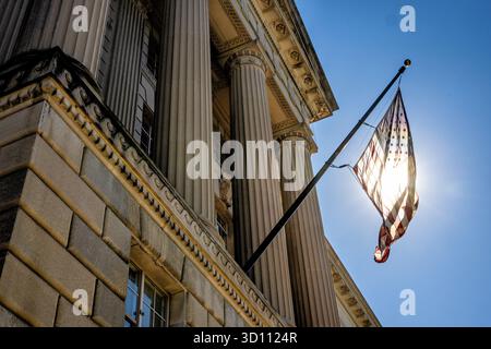 Bandiera DEGLI STATI UNITI retroilluminata dal sole sull'Herbert C Hoover Federal Building Washington DC / WASHINGTON DC - Una bandiera degli Stati Uniti è retroilluminata dal sole sull'Herbert C. Hoover Building, sede del Dipartimento del commercio degli Stati Uniti. Completato nel 1932 in stile neoclassico, l'edificio fa parte del complesso del Triangolo Federale lungo Pennsylvania Avenue NW e prende il nome da Herbert C. Hoover, il 31° presidente degli Stati Uniti. Foto Stock