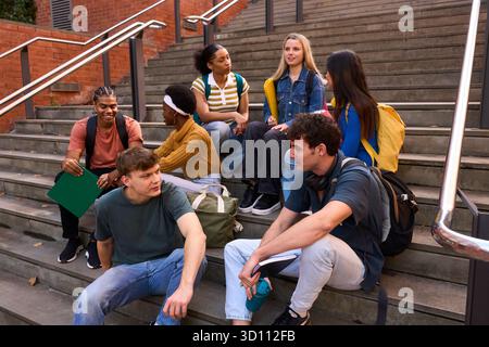 Diversi giovani adulti studiano a parlare sulle scale del campus Foto Stock