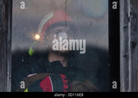 Ritratto vigile del fuoco attraverso la finestra, vigile del fuoco nel casco con torcia guarda fuori, operaio del servizio di soccorso, risposta di emergenza, sicurezza, protezione, eroe Foto Stock