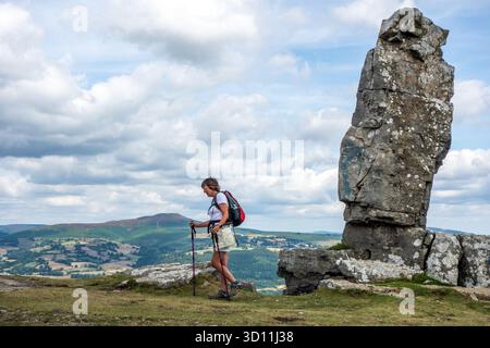Donna con zaino in spalla che passa accanto al Pastore solitario, una formazione rocciosa di pietra calcarea nei Brecon Beacons sopra il villaggio di Llangattock, Galles Foto Stock