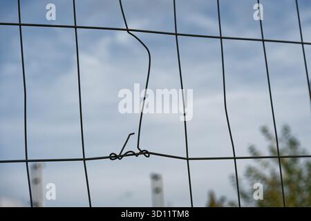 Una recinzione a rete metallica allinea il bordo, un'asta è stata piegata e avvolta su un'altra, l'interruzione ha lasciato una spirale, la riparazione improvvisata mantiene il pannello chiuso, Foto Stock