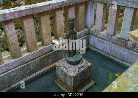 Kyoto, Giappone - 11 ottobre 2025, vista ravvicinata di una piccola scultura in bronzo di un santo saccheggiato in una piccola piscina di pietra, sul territorio di Kiyomizu-dera Templ Foto Stock