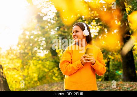 Donna sorridente che indossa un maglione giallo che cammina all'aperto nel parco autunnale Foto Stock