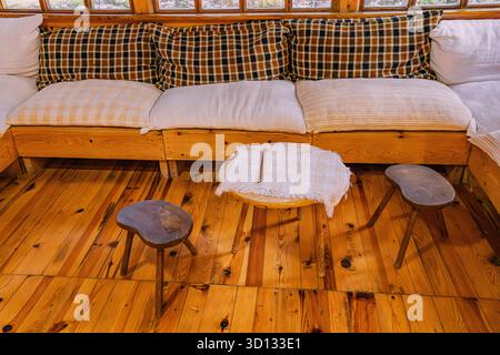 Interni accoglienti che presentano un'atmosfera calda con cuscini a quadri, sgabelli in legno e pavimento in legno naturale, ideale per il relax Foto Stock