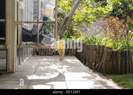 Gambe sporgenti da una finestra, vista giardino Foto Stock