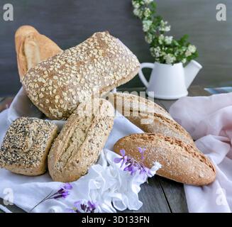 Vari pani artigianali appena sfornati, tra cui cereali integrali e lievito madre, splendidamente disposti su un rustico tavolo in legno Foto Stock